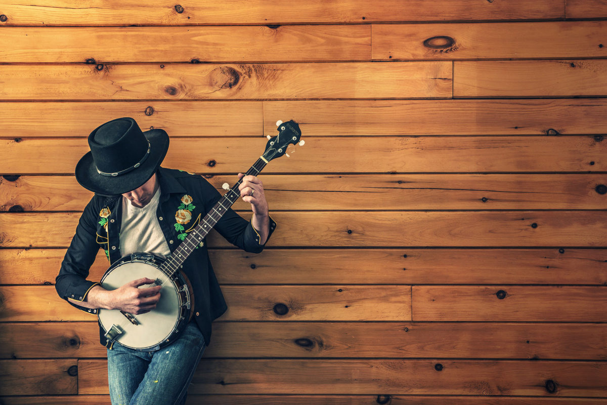 Man playing Banjo and leaning against a wall - What is Creative