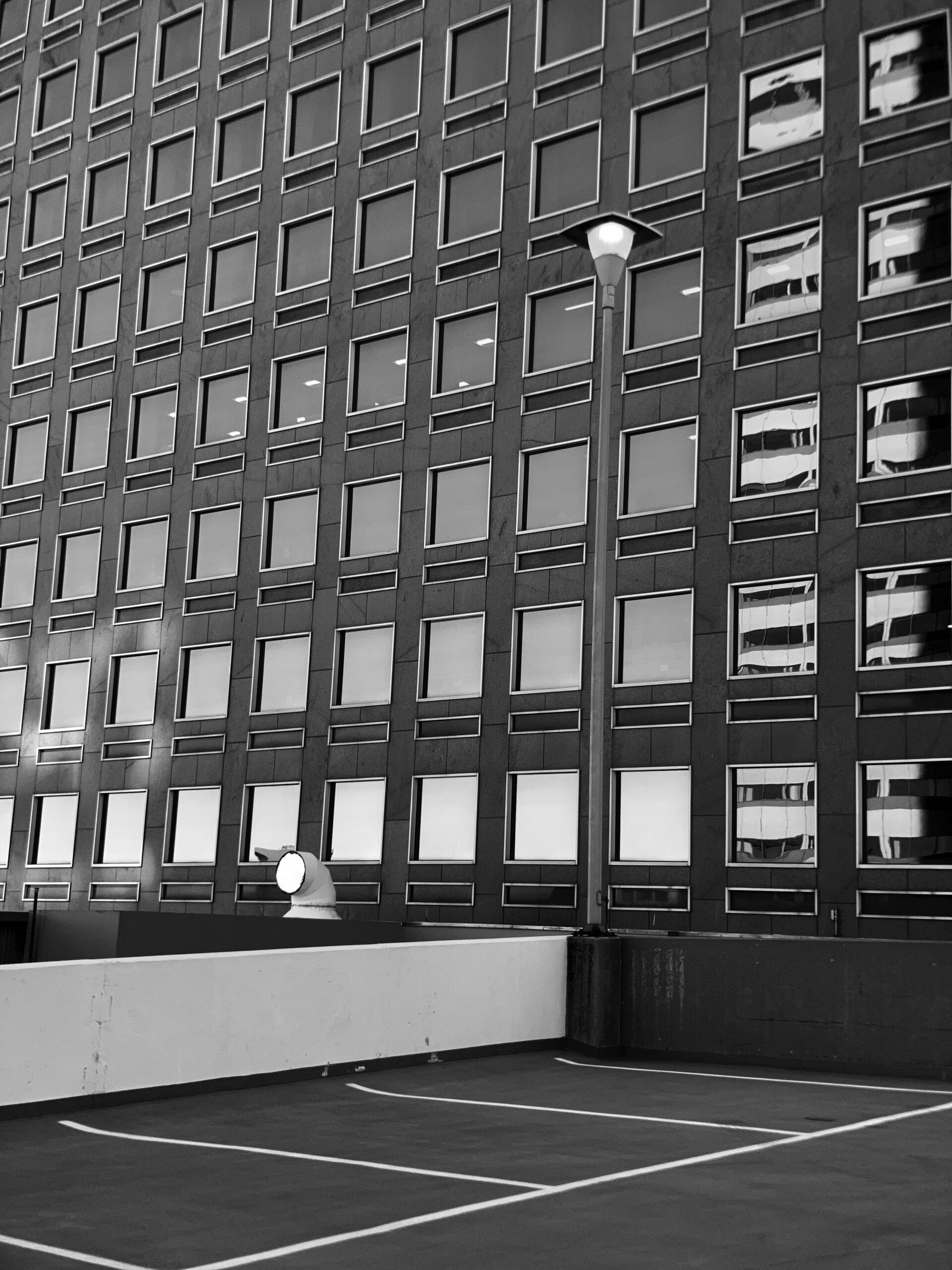 Abstract Black And White Urban Scene with Modern Office Building. architecture, urban, city, black and white, minimalism, building, office, windows, lines, symmetry, geometric, parking lot, design, space, abstract, contrast, monochrome, structure, perspective, industrial, streetlight, reflection, urban landscape, pattern, simplicity, isolated, geometry, row of windows, corporate, exterior, clean lines, vacant, public space, daytime, street architecture, urban design, concrete, texture, office exterior, open area.